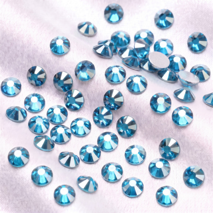 Turkusowobłękitne cyrkonie szklane Aquamarine Satin rozsypane na jasnej tkaninie