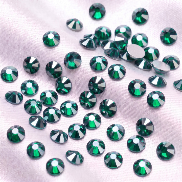 Zielone cyrkonie szklane Emerald Satin rozsypane na jasnej tkaninie