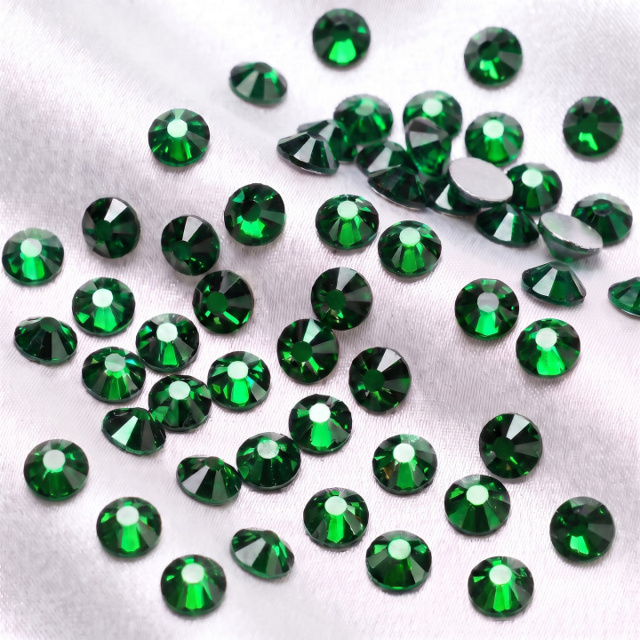 Zielone cyrkonie szklane Emerald rozsypane na jasnej tkaninie