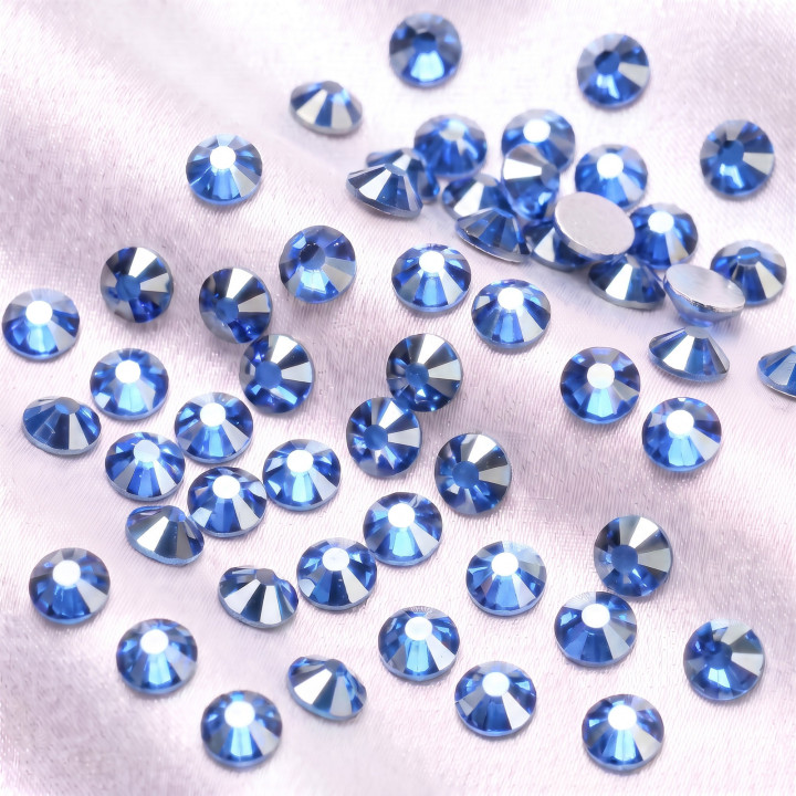 Jasnoniebieskie cyrkonie szklane Light Sapphire Satin rozsypane na jasnej tkaninie